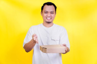 Beyaz gömlekli, gülümseyen bir adam pizza kutusunu parlak sarı arka planda tutuyor. Uluslararası Gıda Günü konsepti