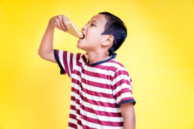 Asyalı genç bir çocuk, parlak sarı bir arka planda, mutlu bir şekilde gülümseyen lezzetli bir dilim pizzanın tadını çıkarıyor. Uluslararası Gıda Günü konsepti