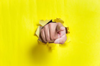 Bir el, yırtık sarı bir kağıdı işaret ederek çarpıcı bir görsel etki yaratıyor.