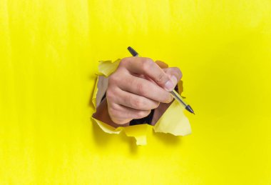 Bir el bir kalem tutar, parlak sarı kağıdı kırıp geçer, yaratıcılığı ve fikirleri sembolize eder..