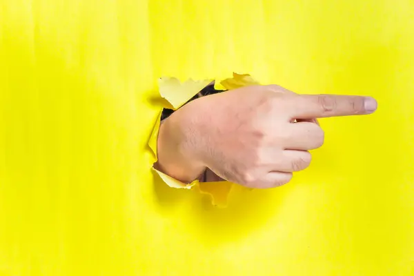 Bir el, yırtık sarı bir kağıdın içinden sağ tarafı gösteriyor ve canlı bir görsel karşıtlık yaratıyor..