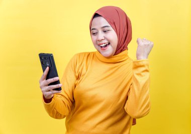 Tesettürlü mutlu bir Asyalı kadın, akıllı telefonuna bakarak heyecanını ve neşesini dile getirir..