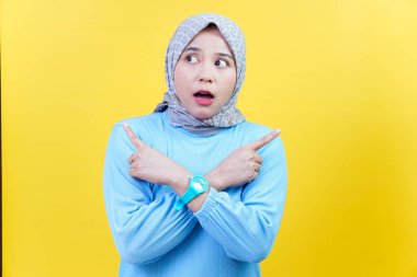 Türbanlı ve mavi elbiseli Asyalı bir kadın şaşırmış ve kafası karışmış görünüyor, zıt yönlere bakıyor..