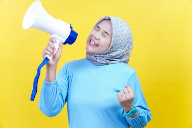 Mavi elbiseli neşeli bir Asyalı kadın elinde bir megafonla sarı arka planda güvenle konuşuyor..