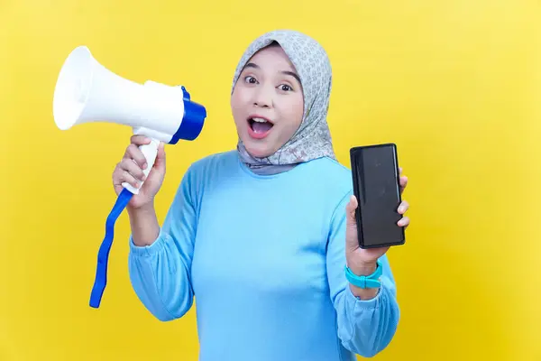 Tesettürlü neşeli bir Asyalı kadın elinde bir megafon ve akıllı telefon tutarak sarı bir arka plana karşı heyecanını dile getiriyor..