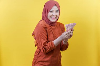 Mutlu bir Asyalı Müslüman kadın tesettüre sarılmış. Parlak bir gülümsemeyle, heyecanını ve finansal başarısını ifade ediyor..