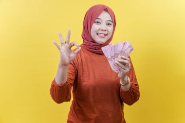 Başörtüsü içinde mutlu bir Asyalı Müslüman kadın nakit tutar ve kendine güvenini ve başarısını ifade ederek iyi bir jest yapar..