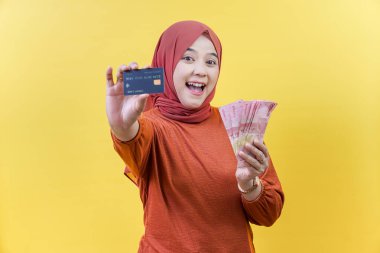 Başörtüsü takan mutlu bir Asyalı Müslüman kadın nakit para ve kredi kartı taşıyor, finansal başarıyı ve akıllıca harcamaları temsil ediyor..