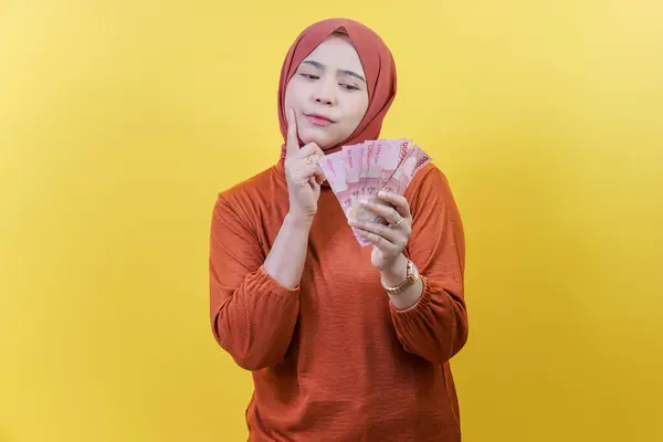 Tesettürlü Asyalı Müslüman bir kadın parasını elinde tutarken nasıl para harcayacağını ya da nasıl yöneteceğini düşünüyor..