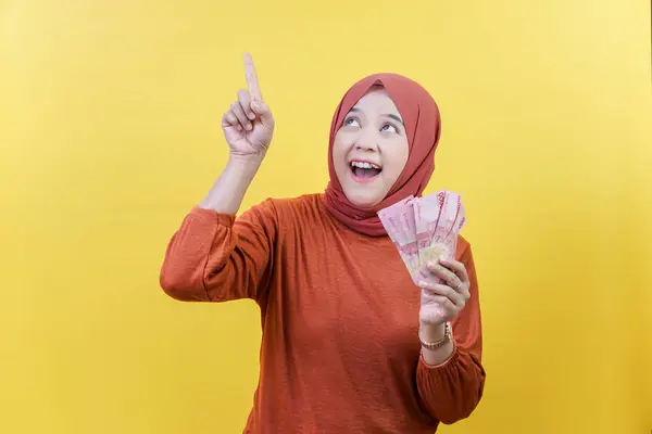 Tesettürlü neşeli bir Asyalı Müslüman kadın elinde para tutuyor ve neşe ve coşkuyu dile getiriyor..