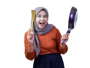 Tesettürlü neşeli Asyalı kadın elinde spatula ve tavayla yemek pişirme pozisyonunda gülümsüyor..