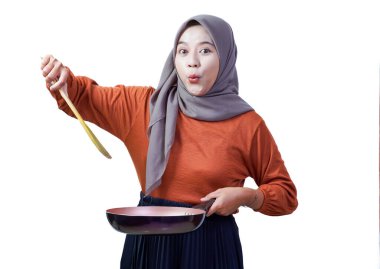 Kızartma tavası ve ahşap spatulayla tesettürlü kadın heyecanını dile getiriyor..