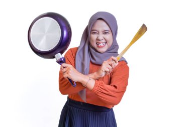 Tesettürlü neşeli Asyalı kadın elinde spatula ve tavayla yemek pişirme pozisyonunda gülümsüyor..