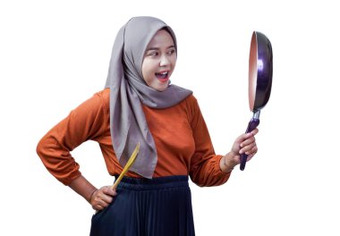 Bir tava ve spatula tutarken gülümseyen tesettürlü Asyalı bir kadın neşe ve merakını dile getiriyor..