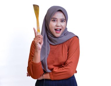 Tesettürlü neşeli bir Asyalı kadın, elinde ahşap bir spatulayla büyük bir gülümseme ile heyecanla bekliyor. Beyaz b parkında izole edilmiş.