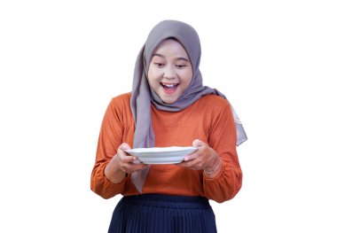 Şaşırmış, tesettürlü Asyalı bir kadın iki eliyle tuttuğu boş beyaz tabağa sevinçle bakar..