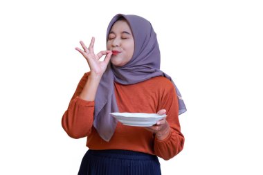 Mutlu bir Asyalı kadın tesettüre girmiş, yemeğin tadını çıkarıyor, tabağı tutuyor ve eliyle nefis bir jest yapıyor..