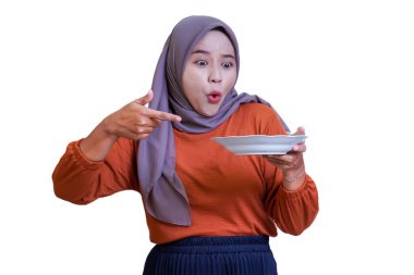 Boş bir tabağa tesettürlü şaşırmış bir kadın heyecanlı bir şekilde tabağa bir şey doğrultuyor.
