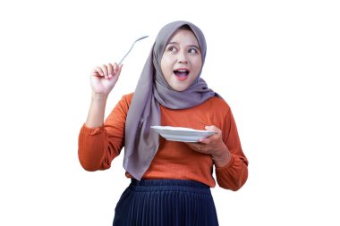 Heyecanlı Asyalı kadın tesettür tabağı ve kaşıkla yukarı bakıyor, neşeli bir ifadeyle, yemeye hazır.