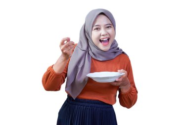 Mutlu Asyalı kadın tesettürlü, parlak gülümseyen, elinde tabak ve kaşıkla, yemeğinin keyfini çıkaracak gibi görünüyor..