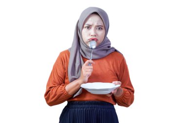 Boş bir tabak ve kaşıkla tesettürlü üzgün Asyalı kadın hayal kırıklığı ve açlığını ifade ediyor..