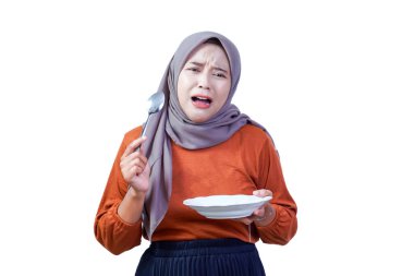 Boş bir tabak ve kaşıkla tesettüre sarılmış ağlayan Asyalı kadın açlık ve üzüntü gösteriyor..