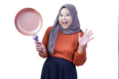 Tesettürlü mutlu Asyalı genç kadın kızartma tavasını tutuyor ve el sallıyor, neşeli yemeklere hazır..