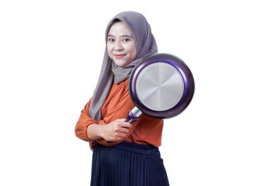 Kendine güvenen, tesettürlü, tesettürlü, tavayı omuzunda tutan, tarzıyla pişirmeye hazır Asyalı genç bir kadın..