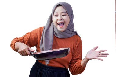 Tesettürlü mutlu Asyalı genç kadın kızartma tavasını tutuyor ve el sallıyor, neşeli yemeklere hazır..