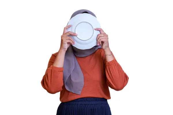 Tesettürlü Asyalı bir kadın beyaz arka planda dururken beyaz bir plaka ile yüzünü kapatıyor..