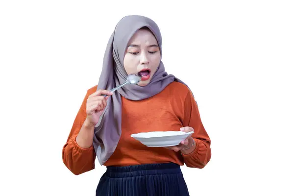 Aç, tesettürlü Asyalı bir kadın. Elinde tabakla boş kaşığa bakıyor ve inançsızlığını dile getiriyor..