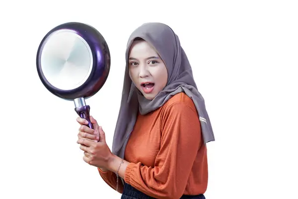 Tesettürlü mutlu Asyalı genç bir kadın kızartma tavasını tutuyor ve el sallıyor, beyaz arka planda izole edilmiş neşeli yemekler yapmaya hazır.