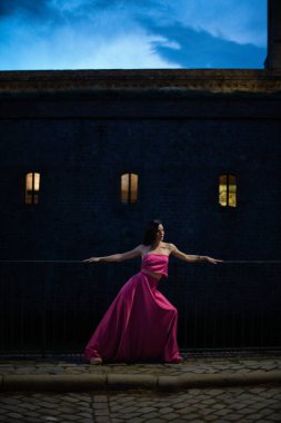 Renkli ve zarif tasarımcı elbiseli bir kadın gece bir şatonun önünde poz veriyor..