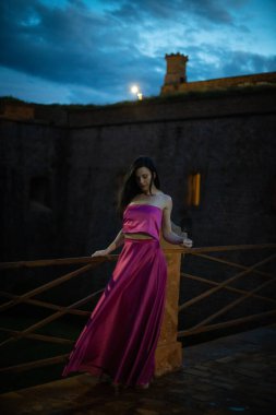 Renkli ve zarif tasarımcı elbiseli bir kadın gece bir şatonun önünde poz veriyor..