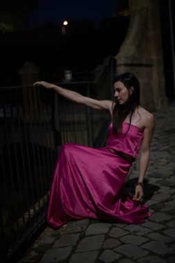 Renkli ve zarif tasarımcı elbiseli bir kadın gece bir şatonun önünde poz veriyor..