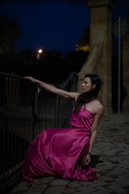 Renkli ve zarif tasarımcı elbiseli bir kadın gece bir şatonun önünde poz veriyor..