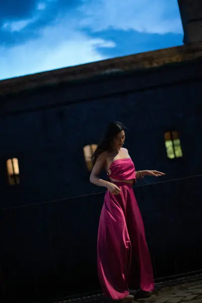 Renkli ve zarif tasarımcı elbiseli bir kadın gece bir şatonun önünde poz veriyor..