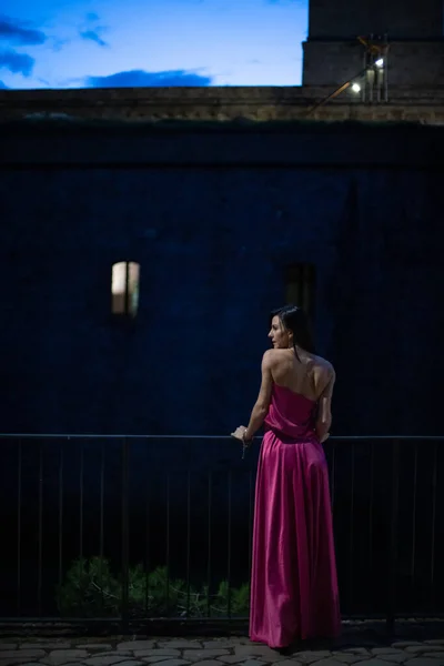 Renkli ve zarif tasarımcı elbiseli bir kadın gece bir şatonun önünde poz veriyor..