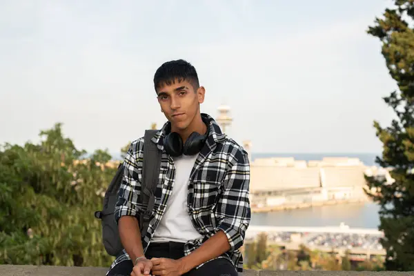 Genç uluslararası öğrenci kampüste çitte oturuyor..