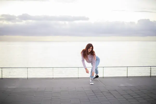 Genç, güzel bir kadın gündoğumunda denizin önünde çağdaş bir şekilde dans ediyor..