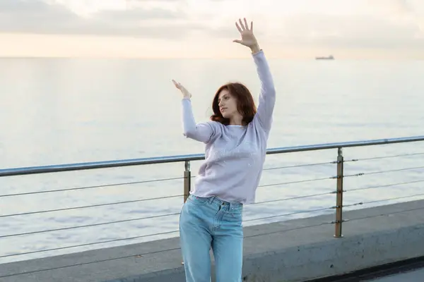 Gün doğumunda denizin önünde dans eden genç kadın..