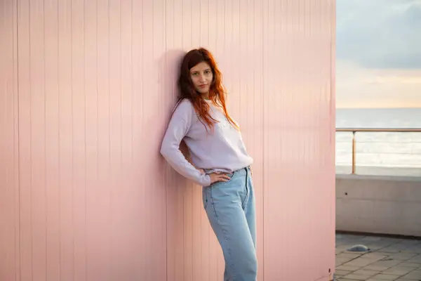 Pembe bir duvarın önünde poz veren manken. Arkaplanda okyanus.
