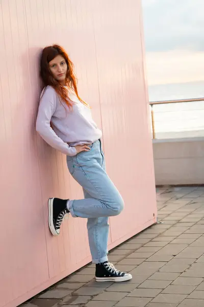 Pembe bir duvarın önünde poz veren manken. Arkaplanda okyanus.