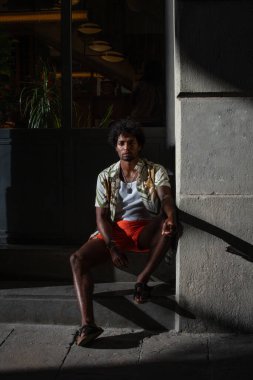  Taştan bir duvarın önünde parlak turuncu mayo ve renkli yaz giysileri giyen Brezilyalı bir model duruyor.. 