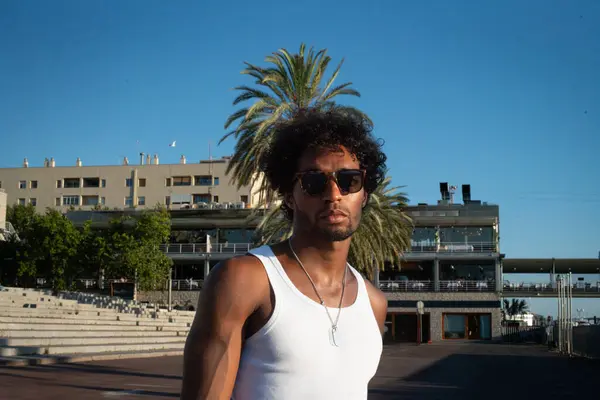 Genç Brezilyalı sporcu, plajdaki bir spor salonunda yoğun bir idman yapıyor, barfiks çekiyor ve parlak turuncu bir mayo giyerken diğer beden eğitimi egzersizlerini yapıyor..