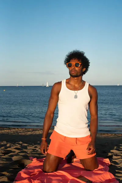 Genç Brezilyalı sporcu, plajdaki bir spor salonunda yoğun bir idman yapıyor, barfiks çekiyor ve parlak turuncu bir mayo giyerken diğer beden eğitimi egzersizlerini yapıyor..