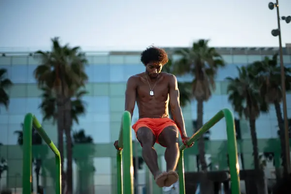 Genç Brezilyalı atlet sahildeki bir spor salonunda yoğun bir idmana katılmış, barfiks çekmiş ve diğer jimnastik egzersizleri yapmış. Turuncu güneşin altında parlak turuncu bir mayo giyerken zayıf ve kaslı vücudunu sergiliyor..