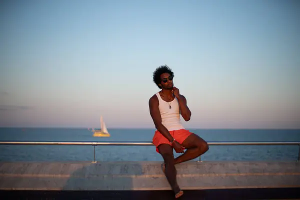  Taştan bir duvarın önünde parlak turuncu mayo ve renkli yaz giysileri giyen Brezilyalı bir model duruyor.. 