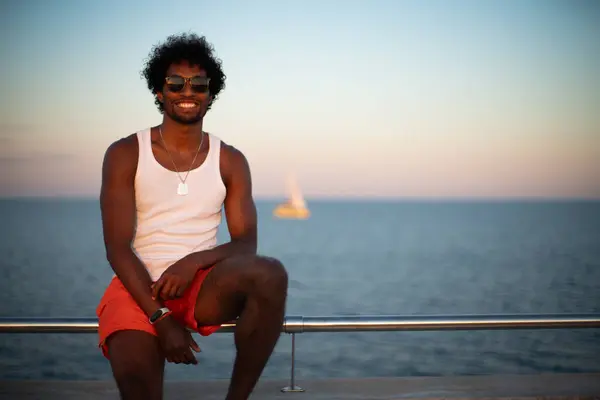  Taştan bir duvarın önünde parlak turuncu mayo ve renkli yaz giysileri giyen Brezilyalı bir model duruyor.. 