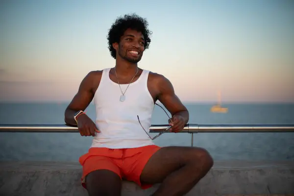  Taştan bir duvarın önünde parlak turuncu mayo ve renkli yaz giysileri giyen Brezilyalı bir model duruyor.. 